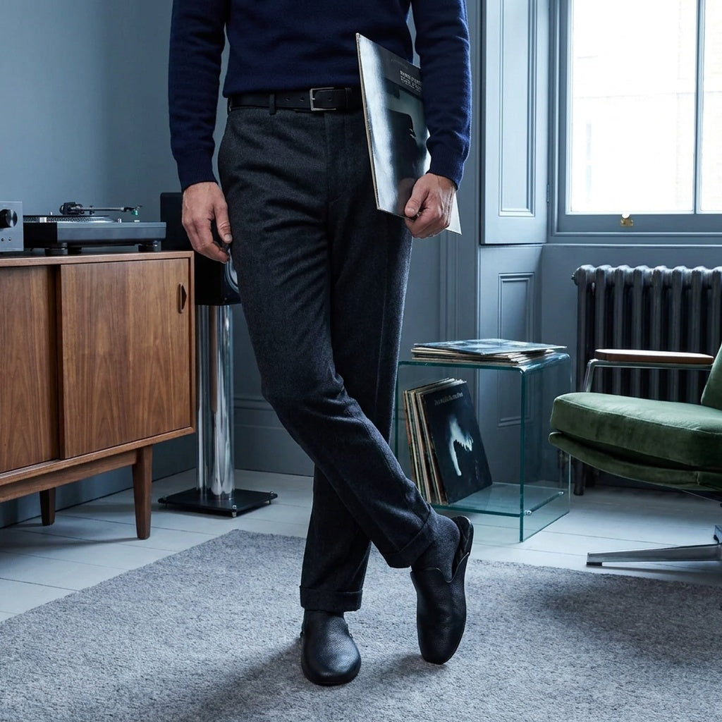 Man in black leather mule slippers by a walnut record cabinet in a blue living room
